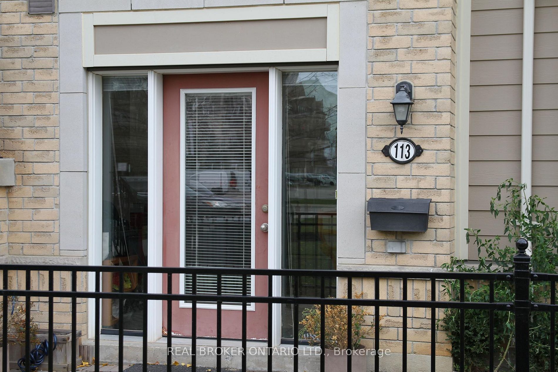 Front entrance of a brick house with a pink front door, glass sidelights, and blinds visible through the door window; house number 113 nearby.