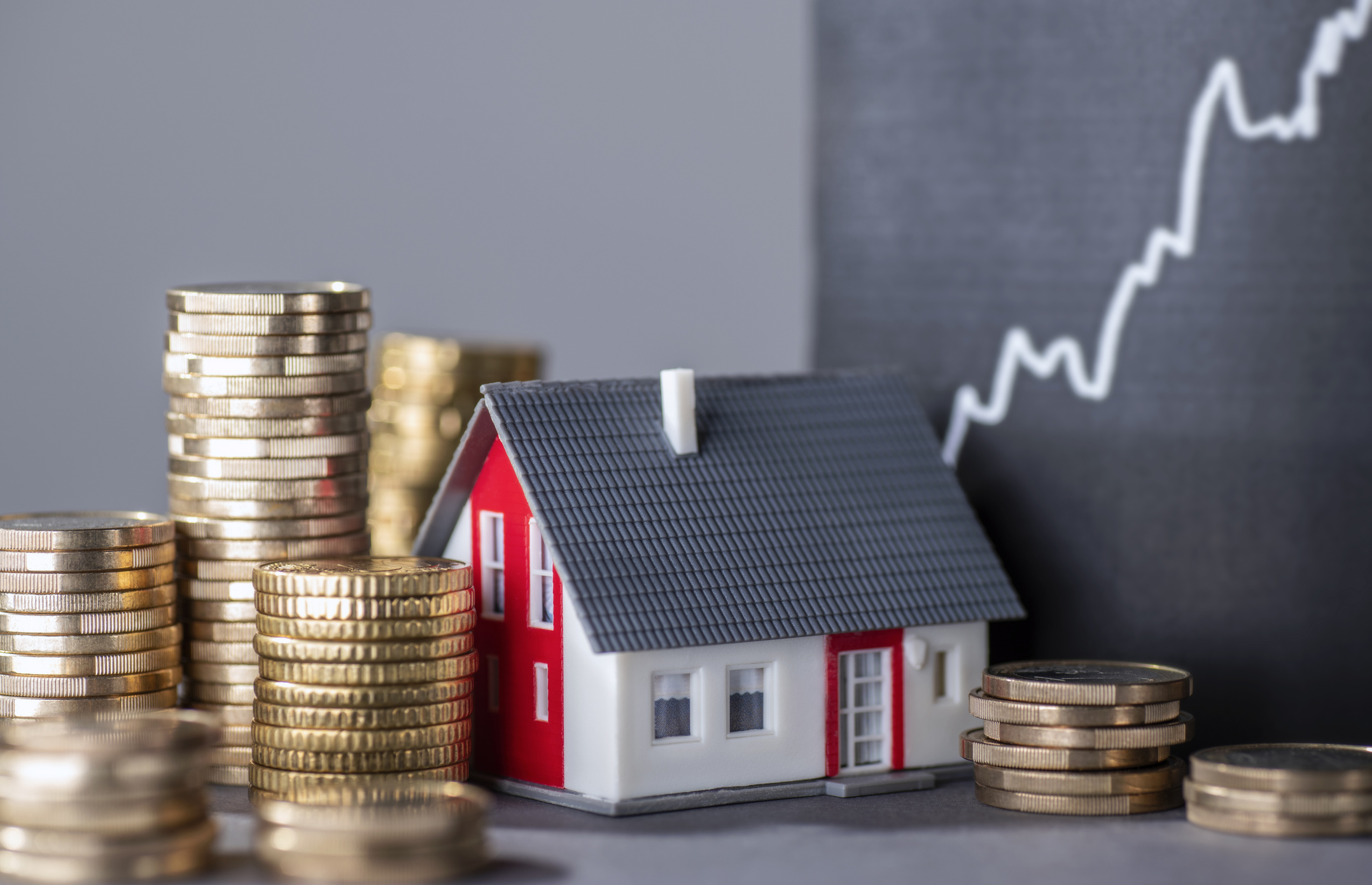 House with stacked coins and a rising financial chart representing home affordability and mortgage qualification in Canada.