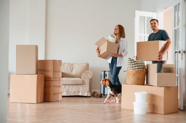 Decluttering Before Moving: Home Staging Tips for a Stress-Free Move A smiling couple carrying moving boxes in a decluttered, well-staged home, highlighting home decluttering tips for a stress-free move.